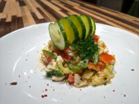 Shopska Salad with diced red and green peppers and creamy feta, topped with a cucumber fan and parsley.