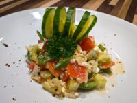 Plated Shopska Salad topped with a folded cucumber fan and a sprig of curly parsley.