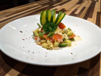 Shopska Salad with diced tomato, cucumber, feta, and green pepper, topped with curled cucumber ribbons.