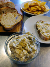 Artichoke Spinach Dip Glass bowl of Artichoke Spinach Dip with bread slices, tortilla chips, and dip on toast.