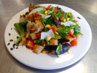 Vinaigrette Salad Vinaigrette Salad with greens, tomato, corn, shaved parmesan, and croutons on a white plate.