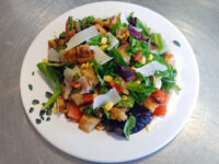 Vinaigrette Salad Vinaigrette Salad with greens, tomato, corn, shaved cheese, and croutons on a leaf-patterned white plate.