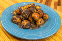 Bobalky with Poppyseeds and Honey piled on a blue plate, coated in poppy seeds with sauce pooling underneath.