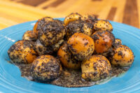 Bobalky with Poppyseeds and Honey piled on a blue plate, dough balls dark with poppy seeds and glossy sauce pooling beneath