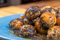 Pile of Bobalky with Poppyseeds and Honey, poppy-seed-coated dough balls glistening on a blue plate.