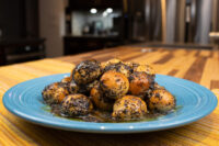 Blue plate piled with round Bobalky dough balls coated in poppyseeds, honey pooling underneath