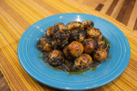Bobalky with Poppyseeds and Honey piled on a blue plate, dough balls coated in dark poppyseed and glazed with honey.