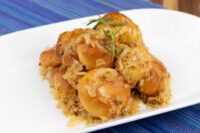 Golden Bobalky with Sauerkraut piled on a white plate, garnished with a fresh herb sprig, set on a blue woven cloth.