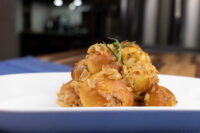 Pile of golden bobalky buns topped with browned sauerkraut and a rosemary sprig on a white plate