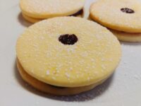 Linzer Tarts Cookies (Linecké Cukroví) stacked in pairs, dusted with powdered sugar, red jam showing through cut-out holes.
