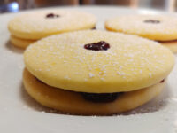 Powdered-sugar-dusted Linzer Tarts Cookies (Linecké Cukroví) with red jam filling on a white plate.