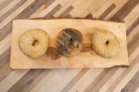Bagel Recipe Three bagels, two with sesame seeds and one dark-seeded, on a live-edge wooden board.