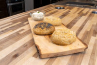 Bagel Recipe Three topped Bagels -- poppy seed, sesame seed, and mixed seed -- on a wooden board with a bowl of cream cheese.