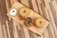 Bagel Recipe Three bagels, two with sesame seeds and one with poppy seeds, rest on a wooden board beside cream cheese.