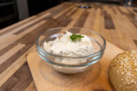 Creamy Spread with Garlic and Chives Glass bowl of Creamy Spread with Garlic and Chives topped with a herb leaf, beside a sesame seed roll.