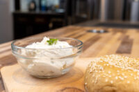 Creamy Spread with Garlic and Chives Glass bowl of Creamy Spread with Garlic and Chives, garnished with herb, beside a sesame seed roll
