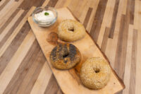 Bagel Recipe Three seed-topped bagels on a wooden board next to a small bowl of cream cheese dip.