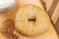 Bagel Recipe A sesame seed-covered bagel on a wood board, with a bowl of herbed cream cheese nearby