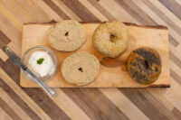 Bagel Recipe Four halved bagels, plain, sesame, and poppy seed, on a wood board beside a bowl of herbed cream cheese