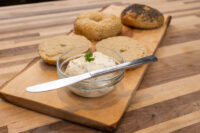 Bagels With Cream Cheese Sesame and poppy seed bagels, halved bagel, and a bowl of cream cheese on a wooden board.