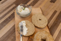 Bagel Recipe Sliced Bagel halves spread with cream cheese beside a sesame Bagel on a wooden board.