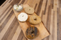 Bagel Recipe Wooden board with four bagel halves, some topped with seeds, beside a bowl of cream cheese