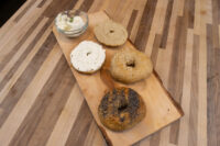 Bagel Recipe Four halved bagels with seeds and cream cheese on a wooden board beside a bowl of herbed cream cheese.