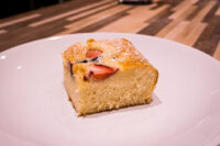 Bublanina (Czech Bubble Cake) Square slice of Bublanina (Czech Bubble Cake) with strawberry slices and powdered sugar on a white plate.