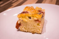 Bublanina (Czech Bubble Cake) Square slice of Bublanina (Czech Bubble Cake) with baked fruit pieces and a glazed top, on a white plate.
