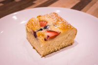 Bublanina (Czech Bubble Cake) Slice of Bublanina (Czech Bubble Cake) with strawberries and dark berries, dusted with powdered sugar, on a plate.