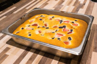 Bublanina (Czech Bubble Cake) Baked Bublanina (Czech Bubble Cake) with strawberries and blueberries in a metal pan on a wooden counter.
