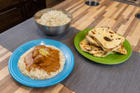Butter Chicken Butter Chicken with rice on a blue plate, beside a bowl of rice and a green plate of flatbread.