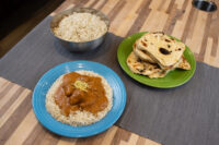Butter Chicken Butter Chicken sauce with meat pieces over rice on a blue plate, beside rice and naan bread.