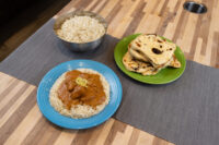 Butter Chicken Butter Chicken with lemon zest over rice on a blue plate, beside a rice bowl and stacked flatbreads.