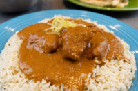 Butter Chicken Blue plate of Butter Chicken: saucy meat chunks in orange-brown gravy over herbed rice, topped with scallions.