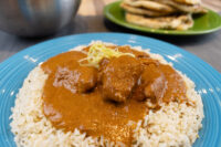 Butter Chicken Butter Chicken chunks in orange-brown sauce over rice on a blue plate, garnished with julienned strips.