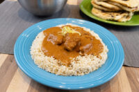 Butter Chicken Butter Chicken pieces in brown curry sauce over rice, topped with citrus zest, on a blue plate.