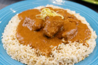 Butter Chicken Butter Chicken chunks in orange-brown sauce over herbed rice on a blue plate, topped with lemon zest strips.
