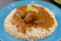 Butter Chicken Butter Chicken pieces in reddish sauce topped with zest, served over herbed rice on a blue plate