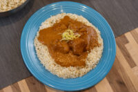 Butter Chicken Butter Chicken chunks in orange-red sauce over rice on a blue plate, garnished with yellow zest.