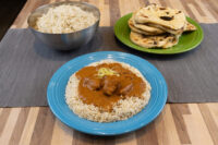 Butter Chicken Butter Chicken with meat in brown curry sauce over rice on a blue plate, beside rice and naan.