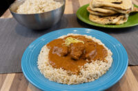 Butter Chicken Butter Chicken over rice on a blue plate, with a bowl of rice and flatbreads beside it.