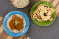 Butter Chicken Butter Chicken curry with rice on a blue plate beside naan bread and a bowl of rice.