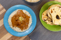 Butter Chicken Butter Chicken with rice and citrus zest on a blue plate, served beside folded naan on a green plate.