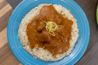 Butter Chicken Blue plate of Butter Chicken, tomato sauce and chicken pieces over herbed rice, topped with citrus zest.
