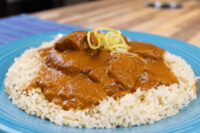 Butter Chicken Butter Chicken in tomato sauce over white rice, garnished with yellow shreds, on a blue plate.