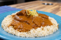 Butter Chicken Butter Chicken with tender meat chunks in tomato sauce over rice, garnished with lemon zest, on a blue plate.