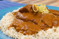 Butter Chicken Butter Chicken pieces in thick brown sauce over rice on a blue plate, topped with yellow shredded garnish.