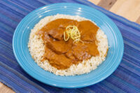 Butter Chicken Butter Chicken pieces in tomato sauce over rice, garnished with julienned strands, on a blue plate