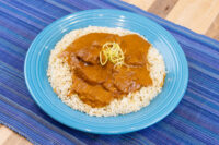 Butter Chicken Butter Chicken pieces in a brown tomato-based sauce served over white rice on a blue plate.
